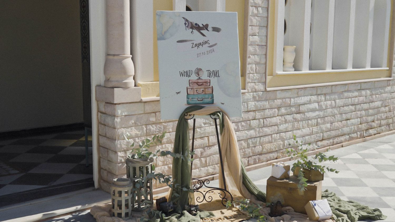 Rustic wedding welcome display with vintage suitcases, lantern, and decorative signage on whitewashed brick porch.