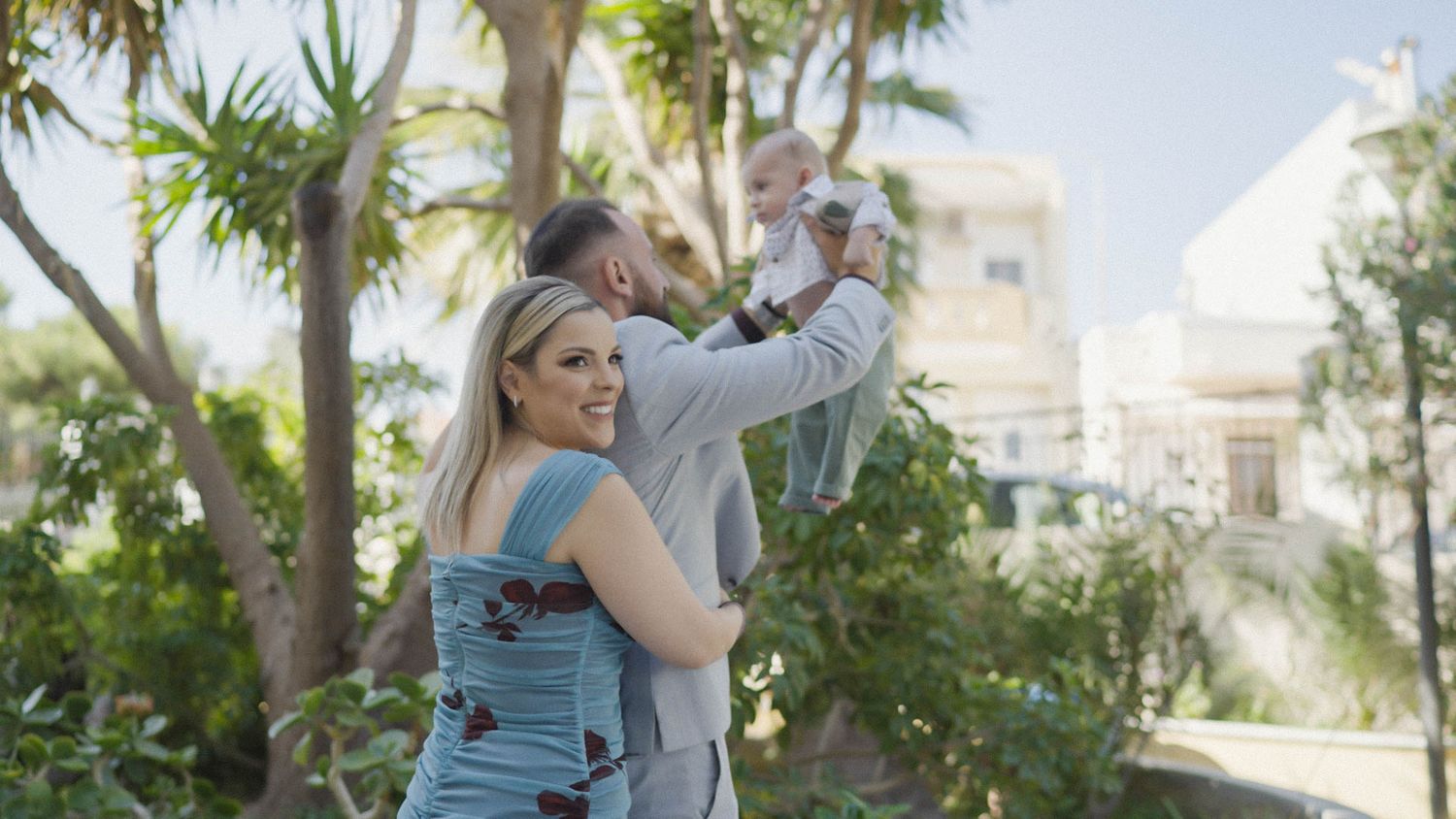 Two people sharing a playful moment together in a tropical garden setting with palm trees and buildings in the background.