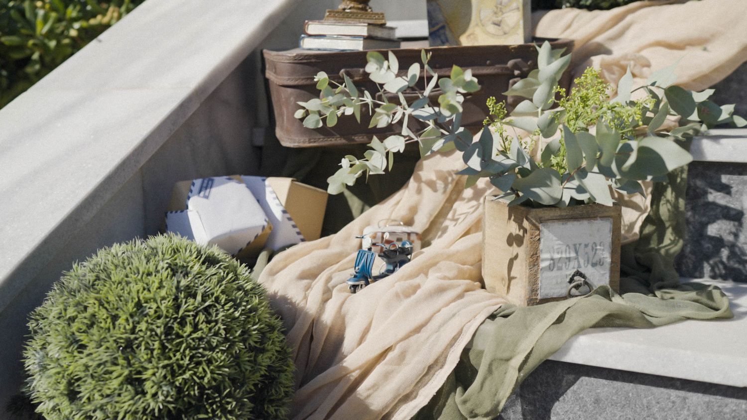 Decorative outdoor table setting with greenery, boxwood topiary, and neutral linens in beige and sage green colors.