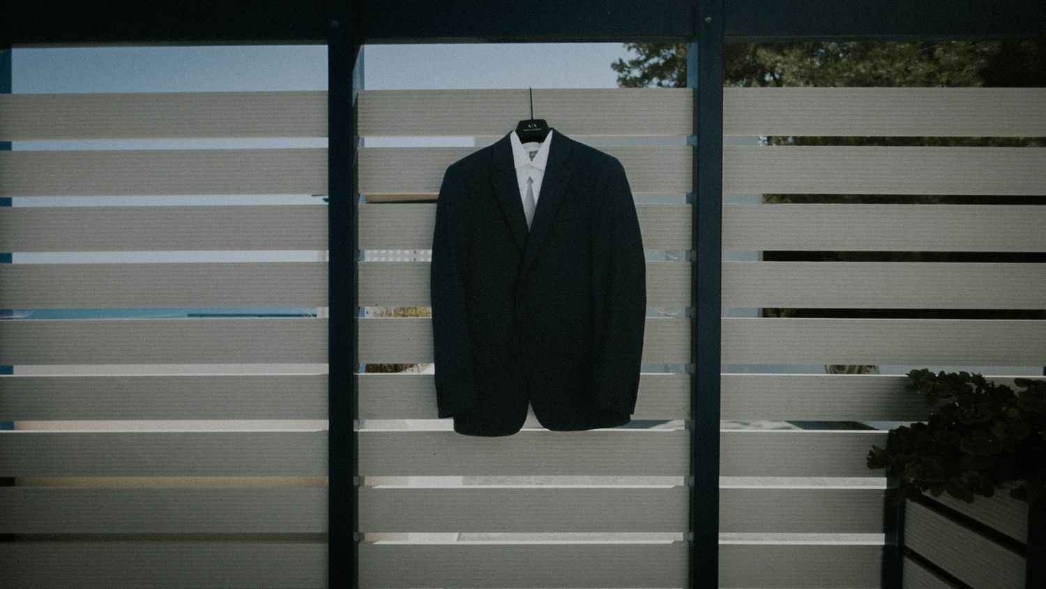 A black tuxedo jacket and bowtie hanging on display against a white slatted wall.