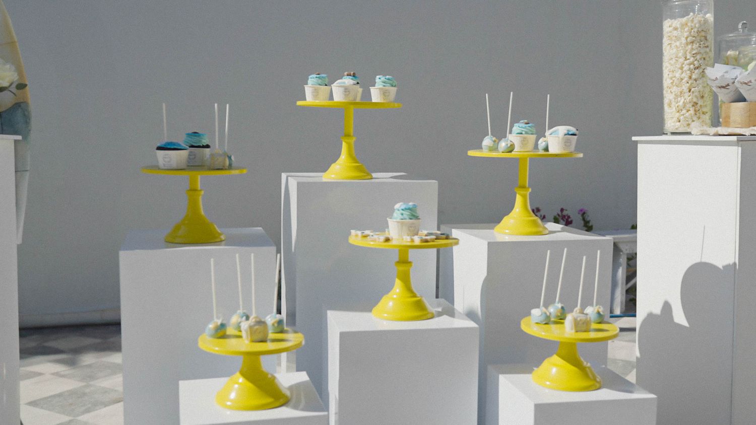 Yellow cake stands display desserts and treats on white pedestals against a gray backdrop.