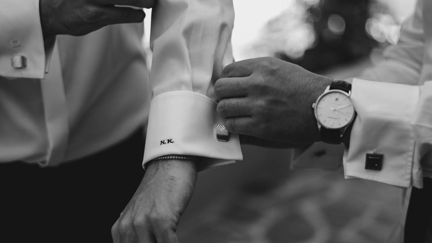 Black and white close-up image of someone adjusting formal cufflinks and wearing a wristwatch.