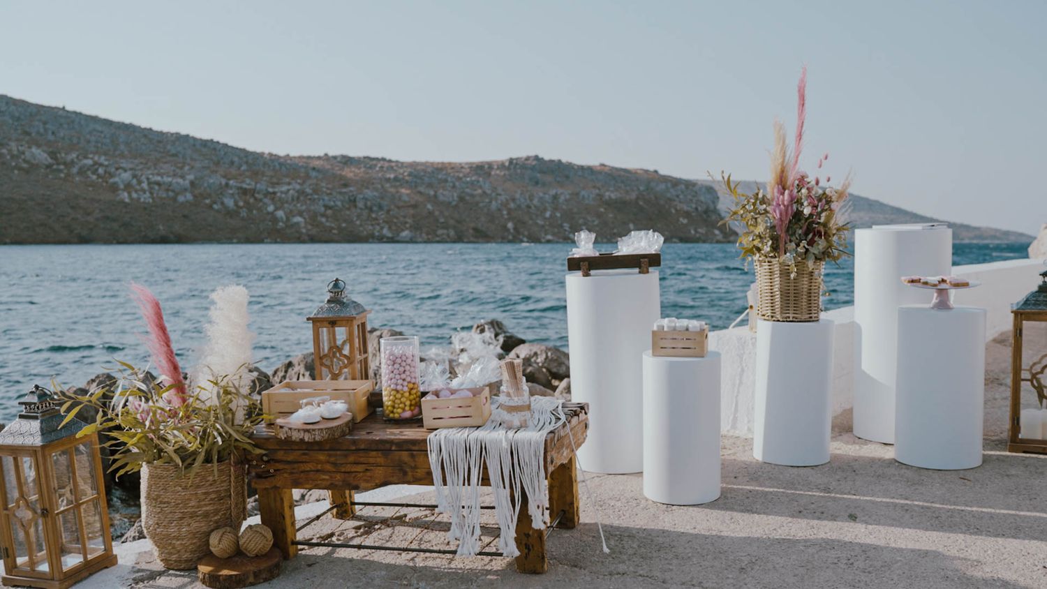 Elegant waterfront wedding reception setup with white pillars and pampas grass decorations overlooking a scenic lake view.