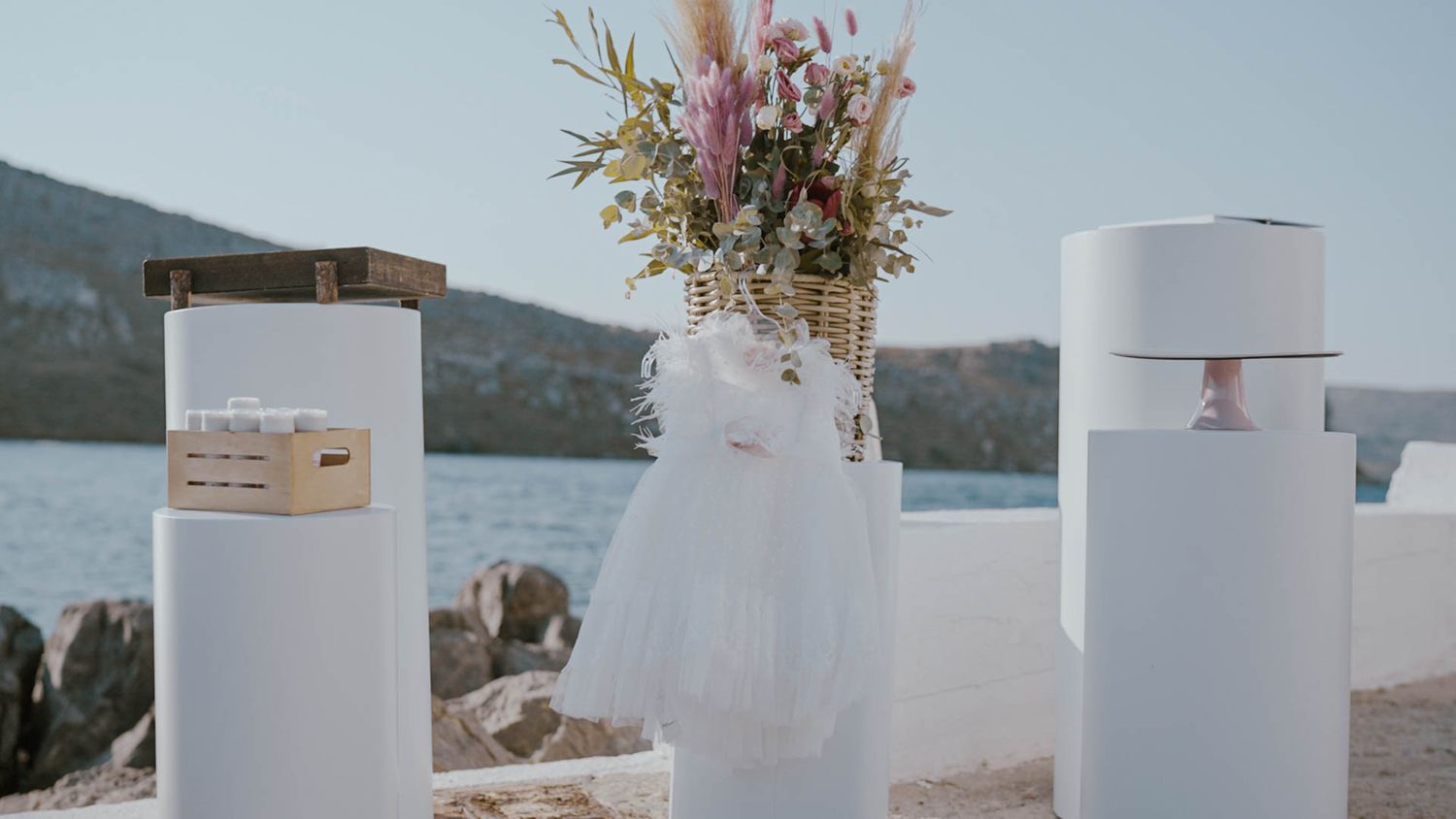 White decorative columns and floral arrangements set up for a waterfront wedding ceremony with mountains in the background.