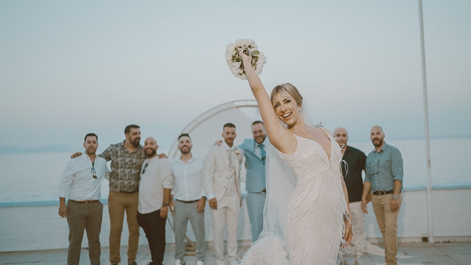 A series of photos showing a beach wedding celebration with a couple and wedding party in white and blue attire on the sand.