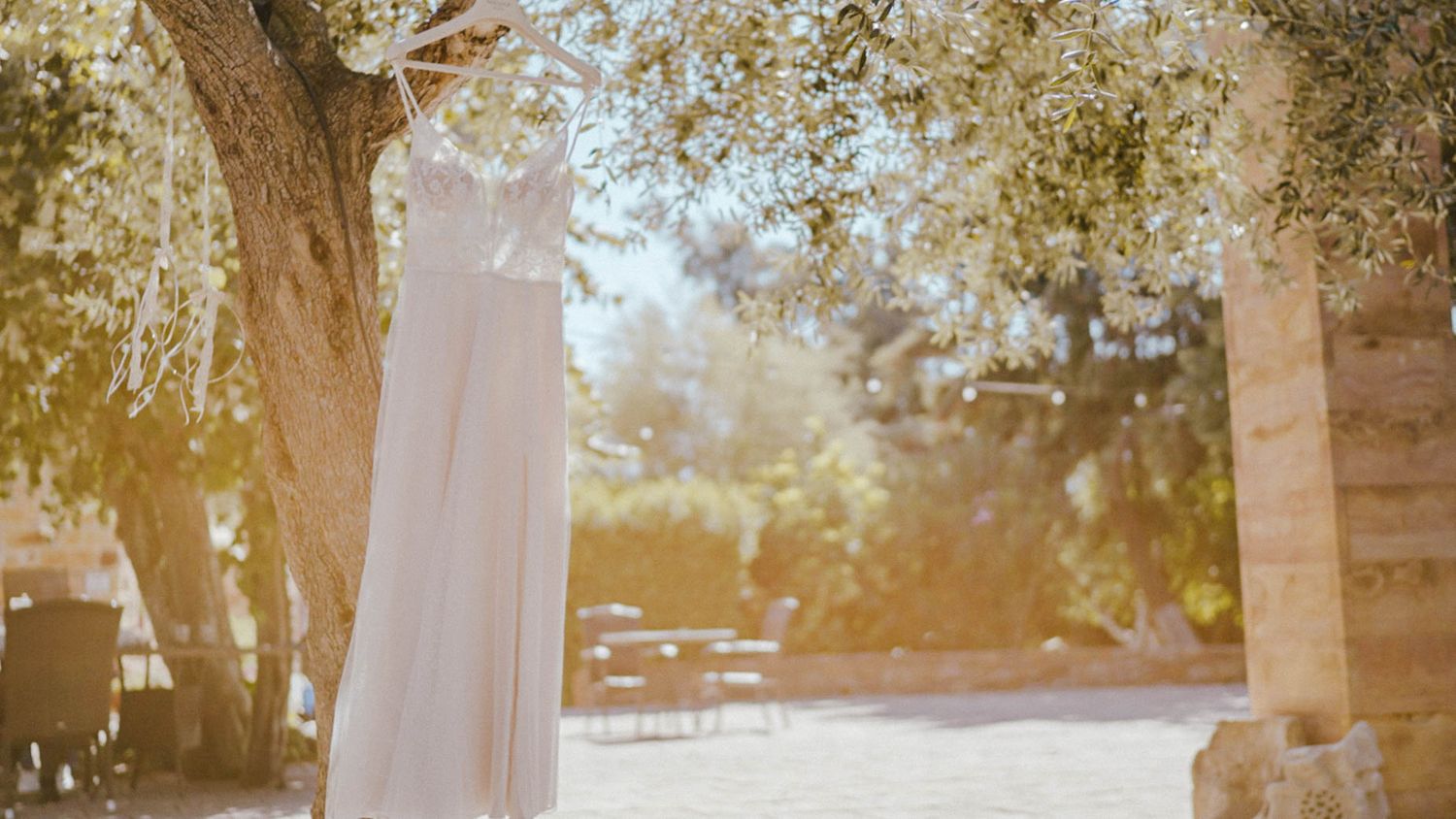 A white flowing curtain hangs between trees in a sunlit outdoor setting creating an ethereal wedding arch.