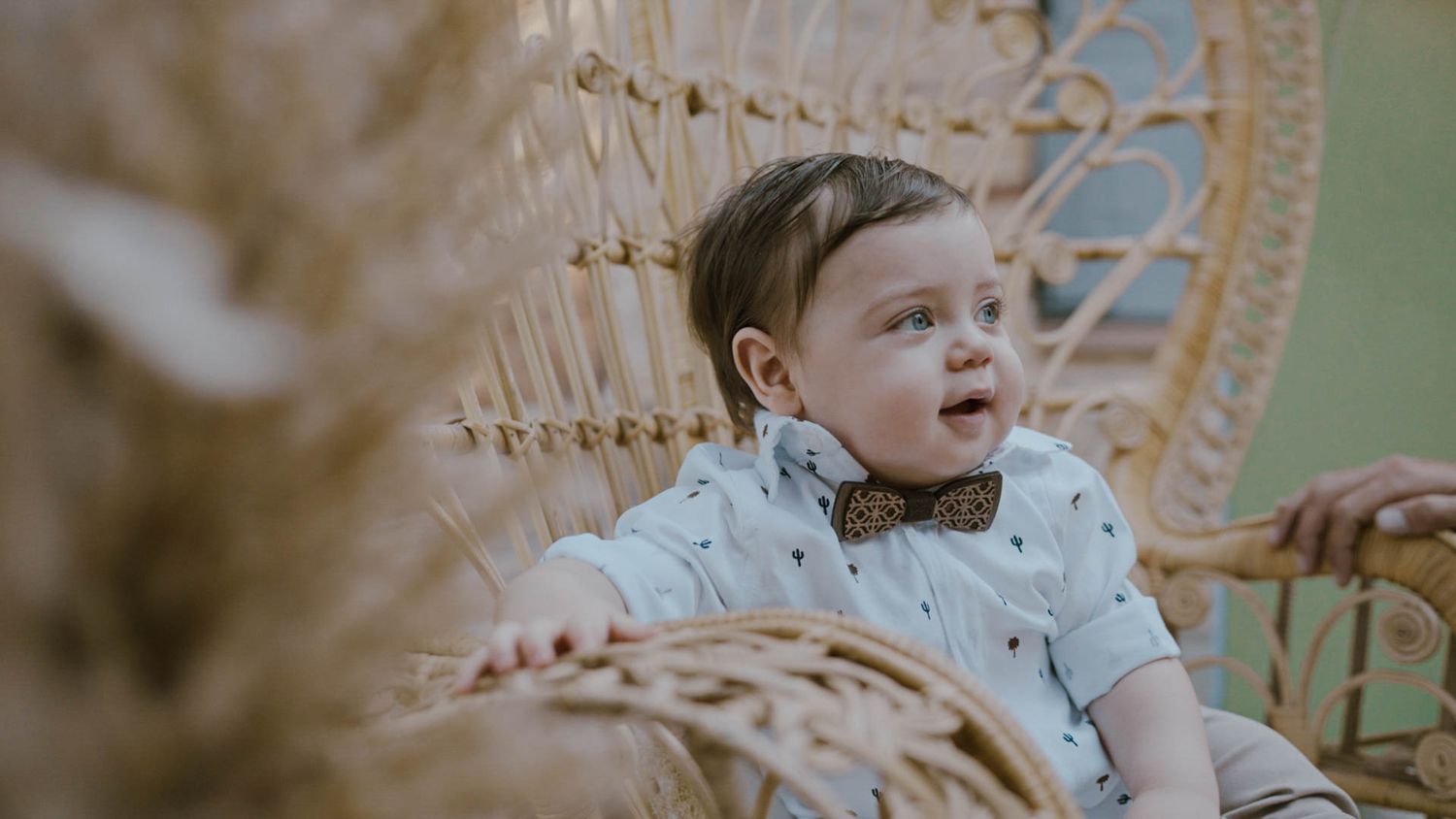 A small child sits in a woven wicker peacock chair, looking to the side with an expression of wonder.