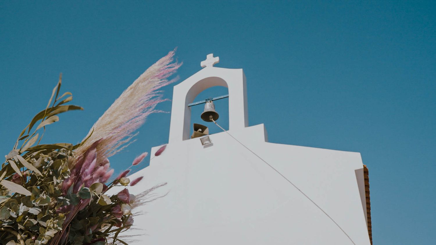 Traditional white Greek church bell tower with a single bell against bright blue sky in warm Mediterranean light.