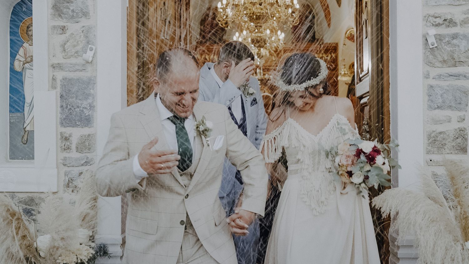 Joyful wedding couple celebrating with confetti outside a stone building with elegant decor.