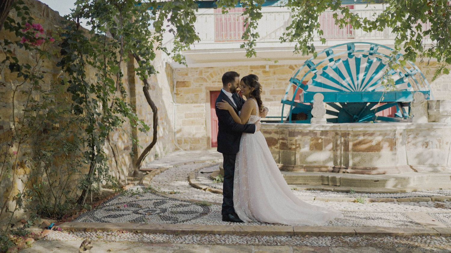 Couple embraces in a romantic garden courtyard with turquoise art wall decor and hanging greenery.