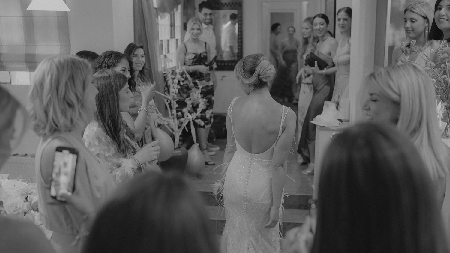A woman in a sleeveless dress stands among a group at a social gathering, captured in black and white.