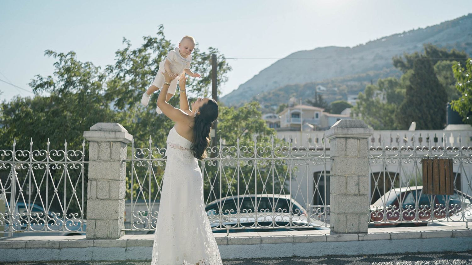A pair of champagne glasses clink together in a toast against a scenic mountain backdrop with ornate white railings.