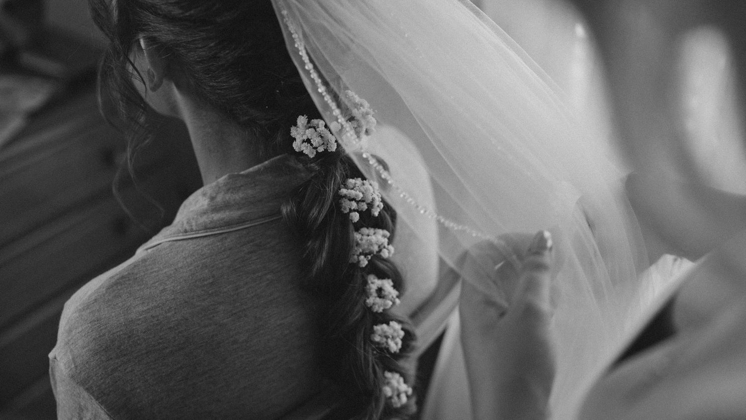 Black and white close-up of a bride's back showing details of her wedding dress and delicate floral hair decoration.