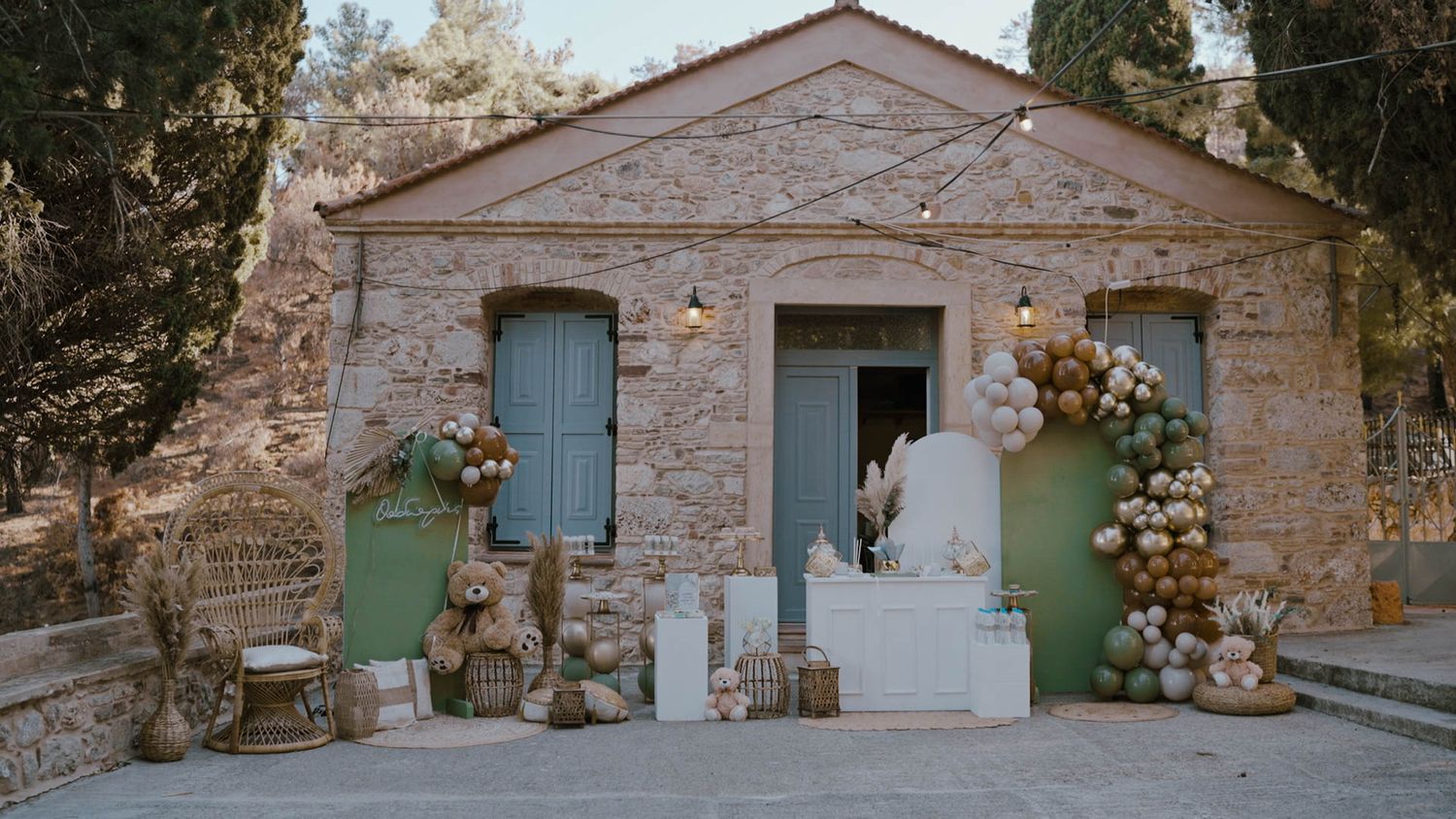 A rustic stone building with blue and green doors decorated with elegant floral arch arrangements and lanterns.