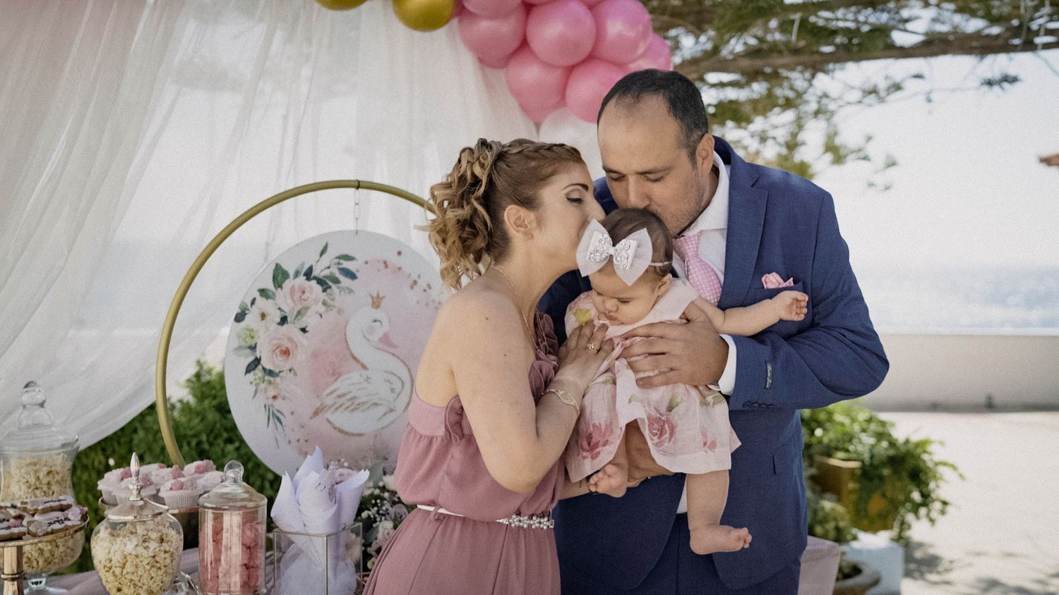 Family celebrates special moment together at elegant outdoor party with floral decorations and pastel pink balloons.