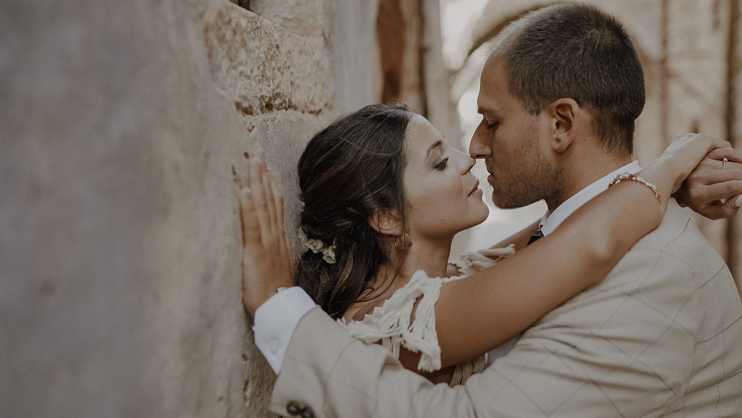 Romantic close-up of wedding couple embracing against stone wall.