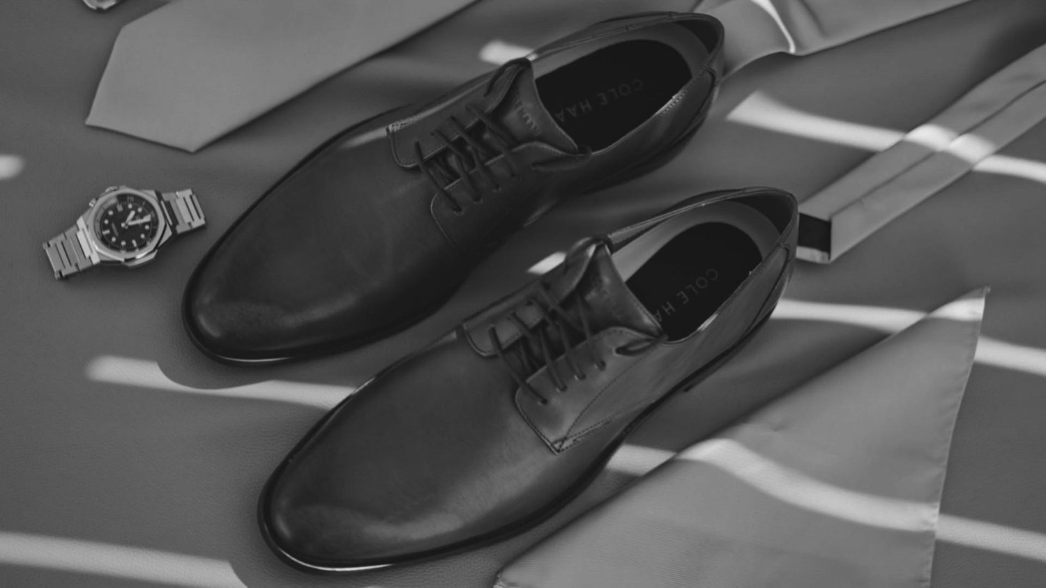 A pair of black leather oxford dress shoes positioned on a gray surface in black and white monochrome.