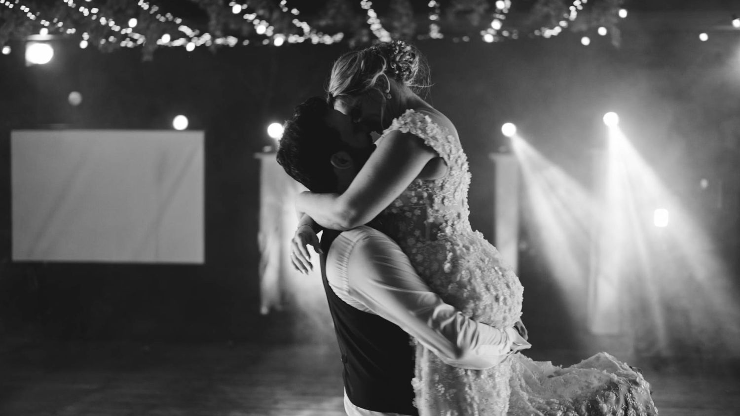 A performer in a bodysuit dances with dramatic stage lighting and spotlights in a black and white photo.