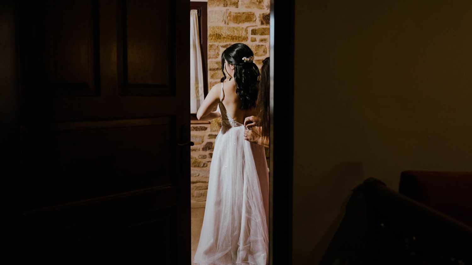 A silhouetted figure stands in a doorway wearing an elegant white wedding gown against exposed brick walls.