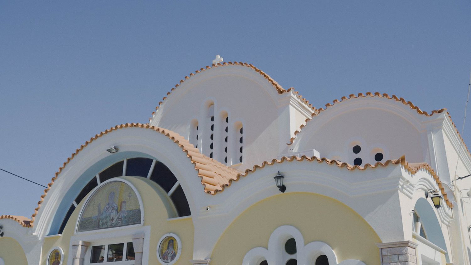 Architectural detail of a white Mediterranean-style building with arched windows and decorative scalloped roofline against blue sky.