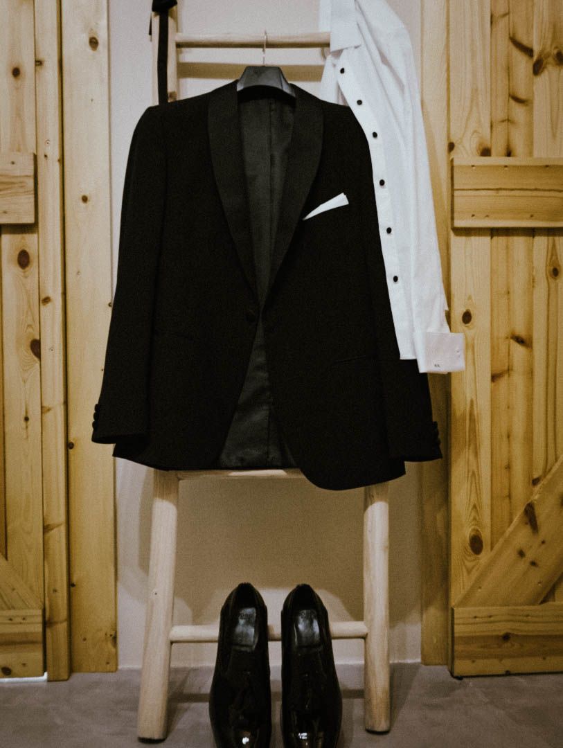 A formal black suit jacket hanging on a wooden closet with black dress shoes placed neatly beneath.