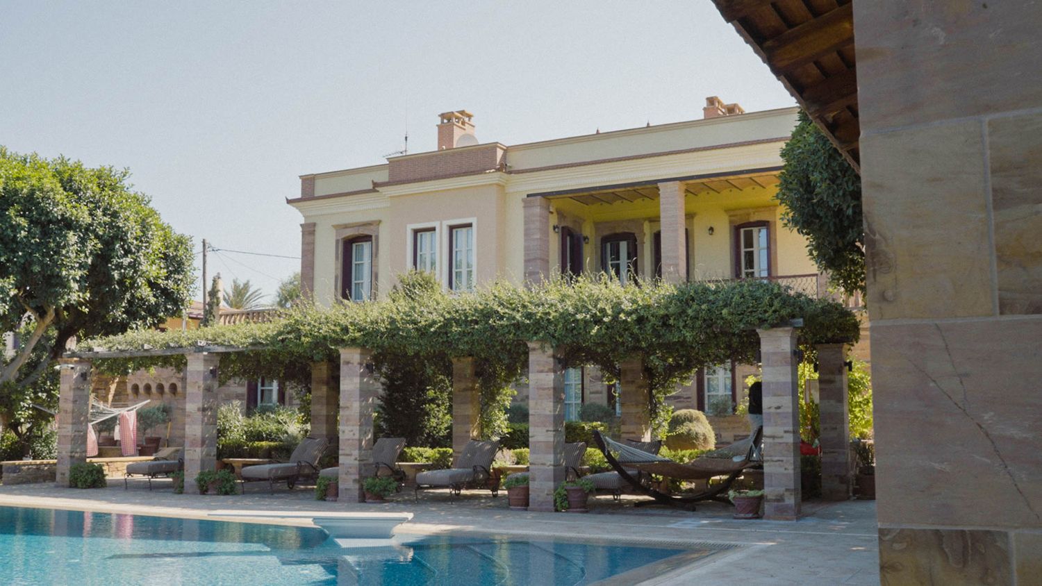 Elegant Mediterranean villa with covered stone patio, swimming pool and climbing vines overlooking a sunny terrace.
