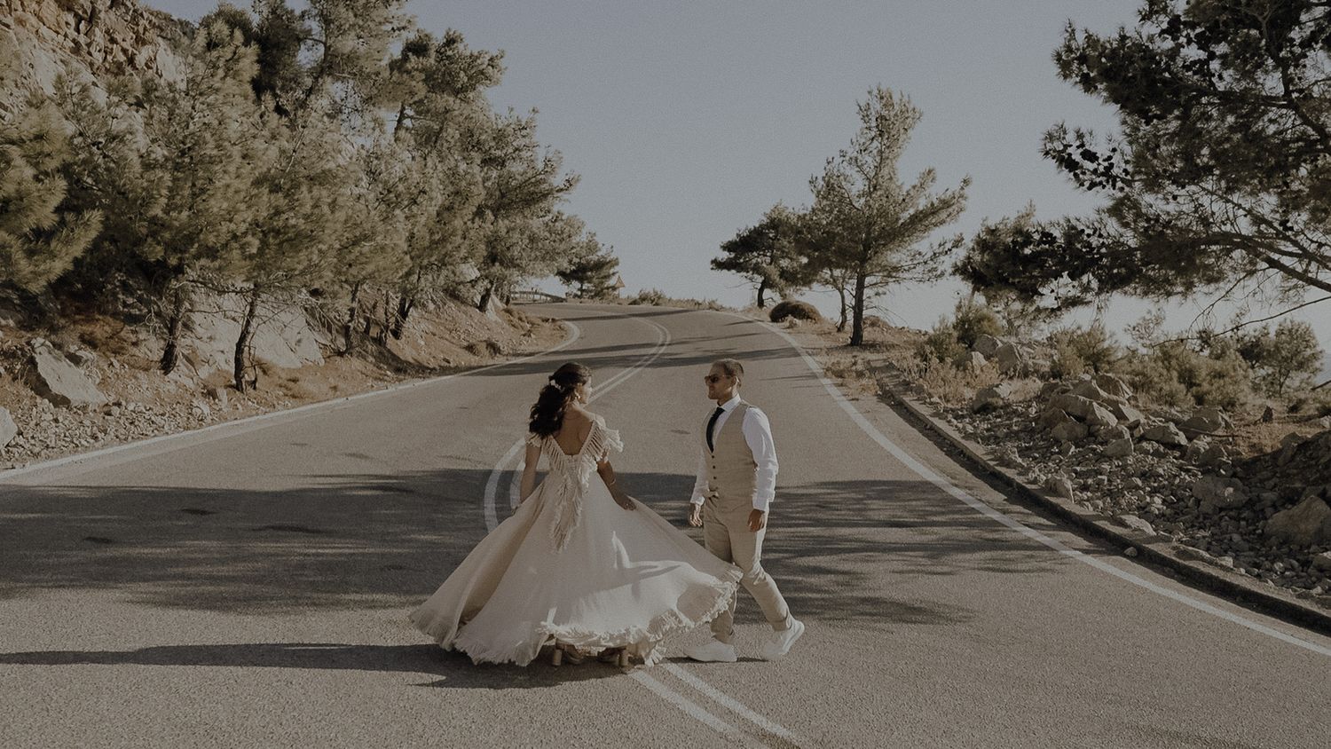 Wedding couple dancing on empty mountain road surrounded by pine trees.