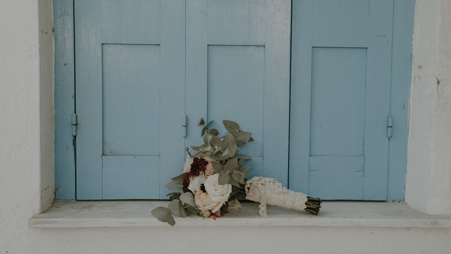 Wedding bouquet with white flowers and greenery placed against pale blue doors.