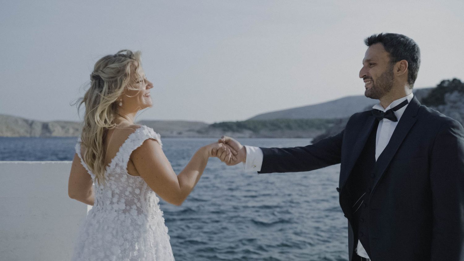 A bride and groom dancing together on a coastal cliff overlooking the blue ocean waters.