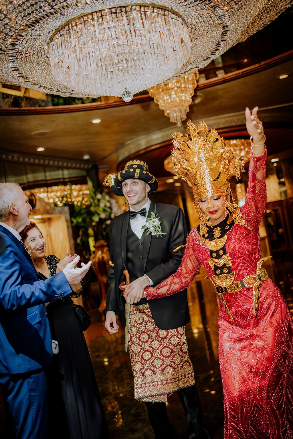 Wedding guests dance elegantly under ornate crystal chandeliers at a traditional Indonesian celebration.