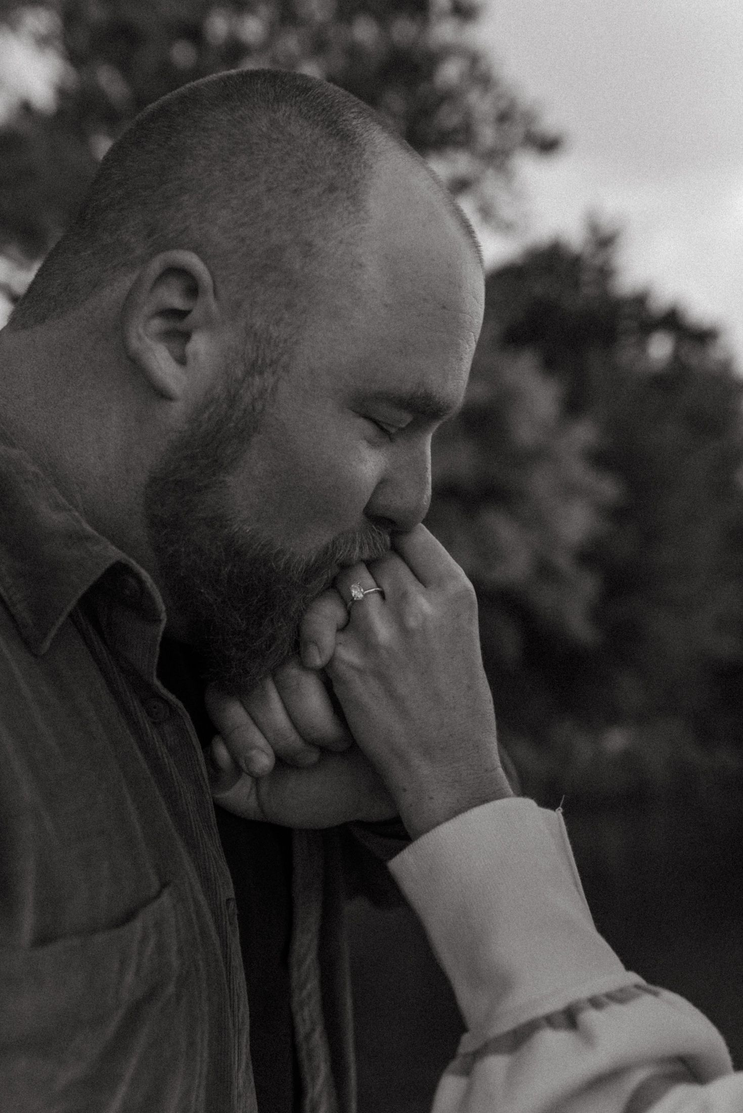 Black and white artistic portrait of two people embracing in a candid emotional moment outdoors.