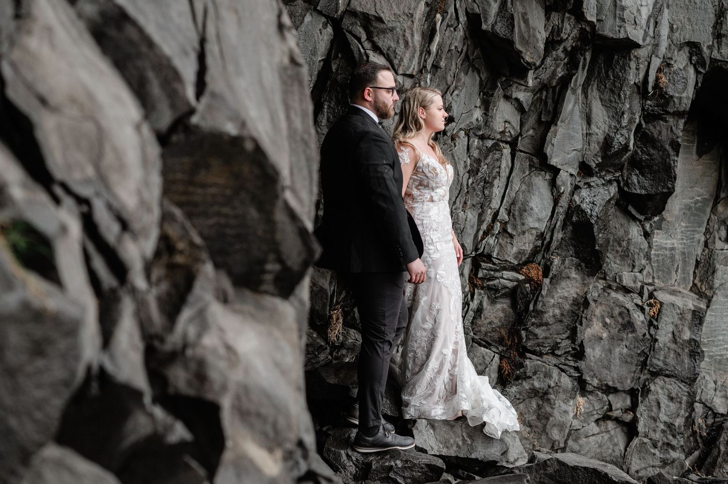 A romantic wedding couple poses against dramatic black volcanic rocks on a moody, overcast day.