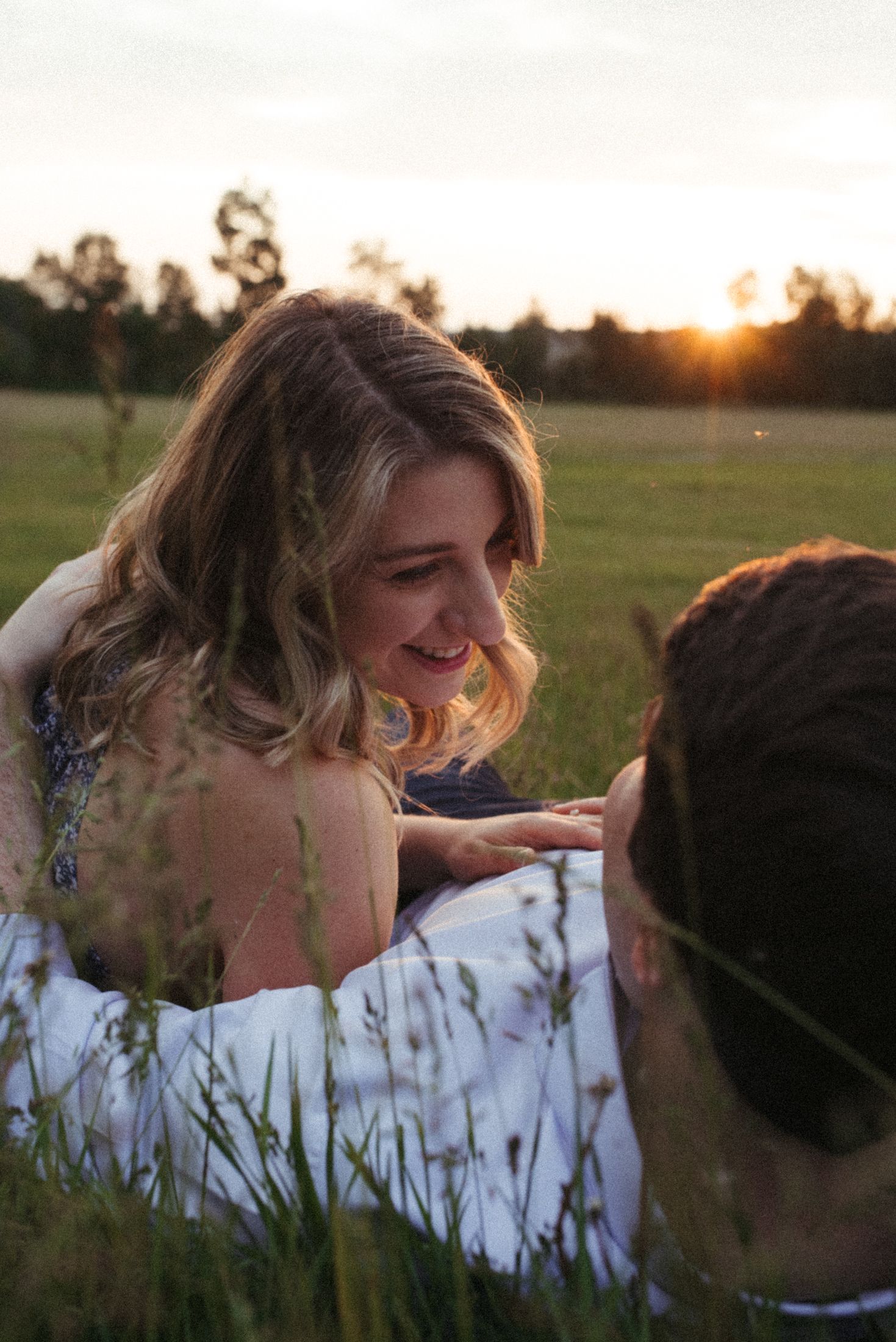 A romantic sunset scene in a grassy field with a white-dressed woman smiling during a photoshoot.