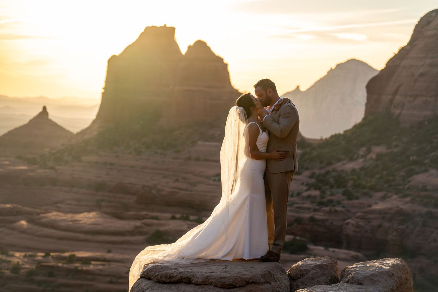A couple shares an intimate wedding moment atop red rock formations at sunset in Sedona, Arizona.