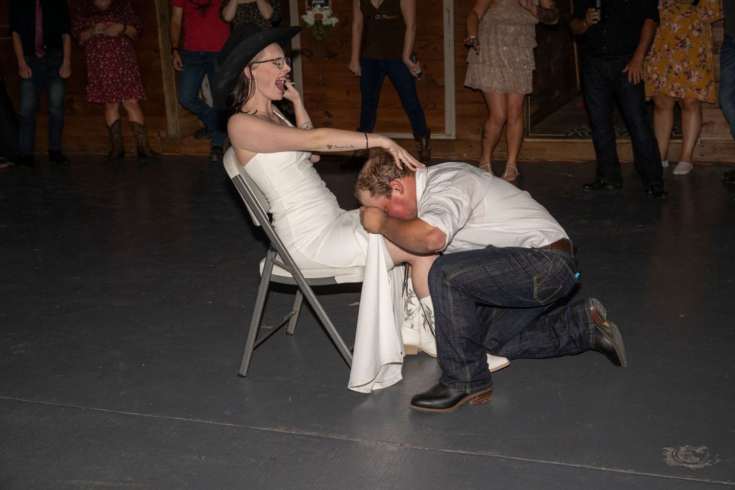 Wedding guests participate in the traditional garter removal dance during a reception at an indoor venue.