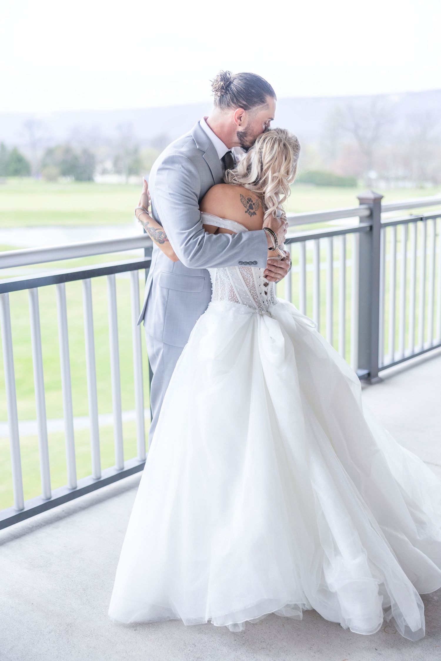 A romantic wedding moment captured on a covered balcony overlooking scenic mountain views as couple embraces in formal attire.