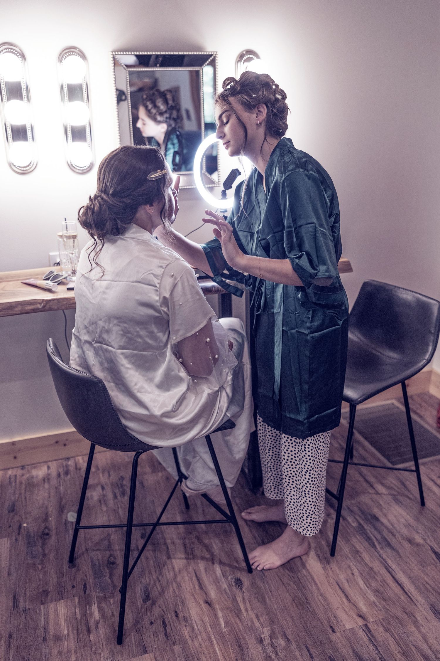 A makeup artist applies cosmetics in a dressing room with bright vanity lighting and a modern minimalist decor.