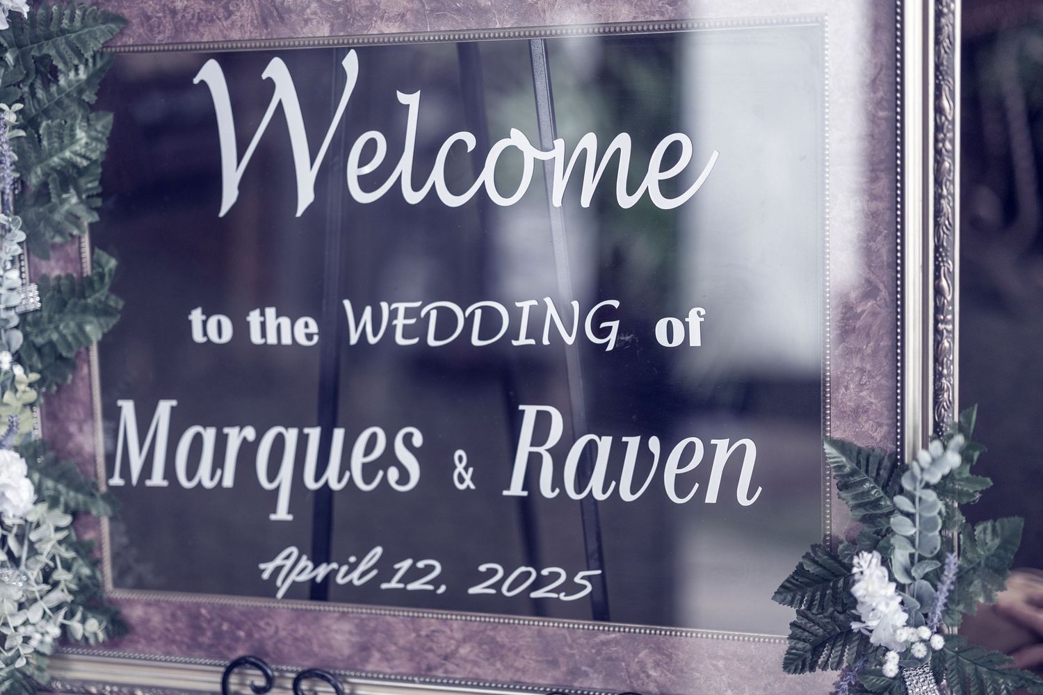 A wedding welcome sign with purple tones displays 'Welcome to the Wedding of Marques & Raven' with the date April 22, 2023.