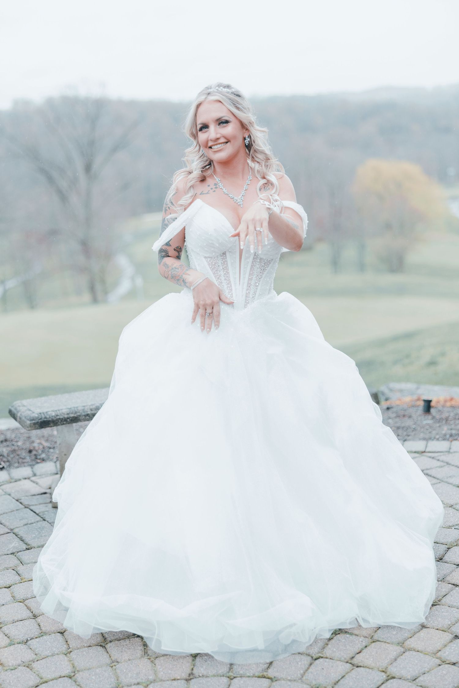 Bride in strapless ballgown with corset bodice and full tulle skirt poses outdoors on stone patio with rolling hills behind.