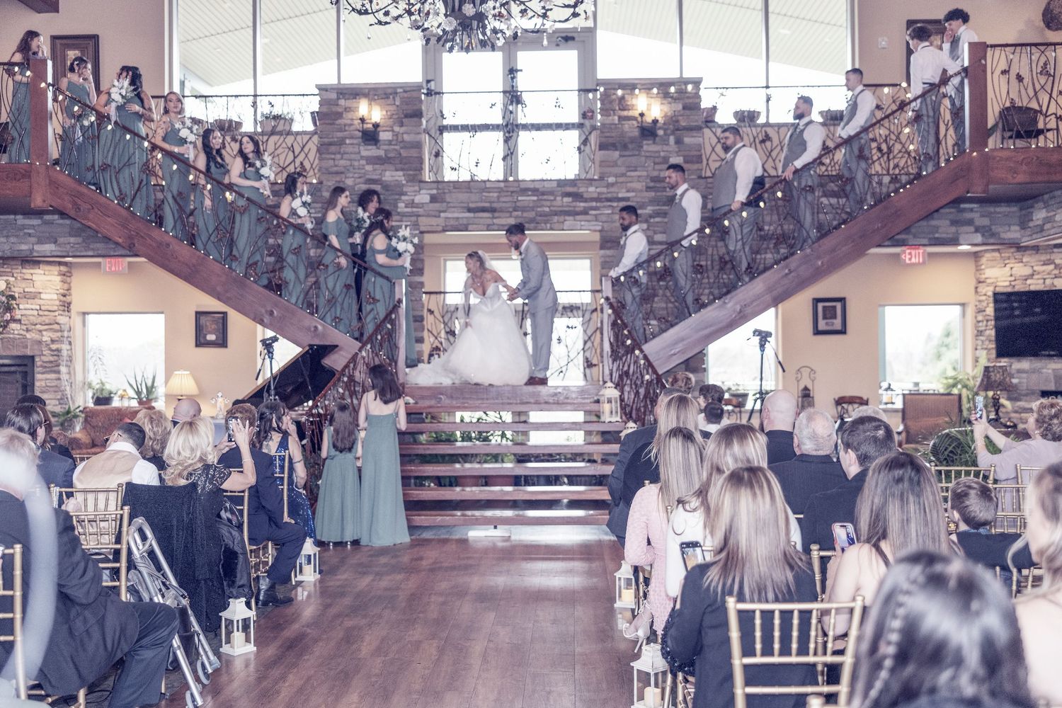 A grand staircase entrance at a wedding venue with guests gathered on both sides in an elegant rustic setting.