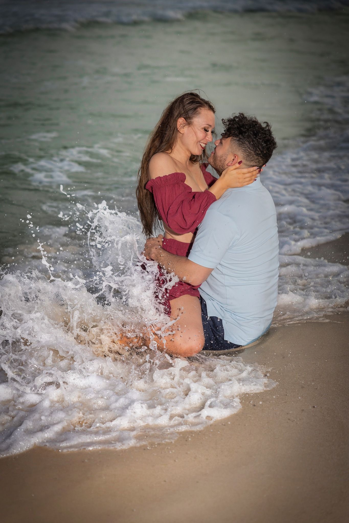 Couple embracing in ocean waves during beach photoshoot.