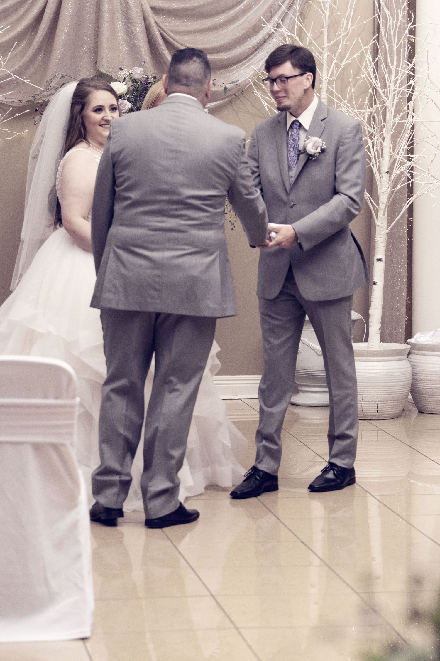 Wedding ceremony in progress with officiant and couple in formal attire surrounded by white decor.