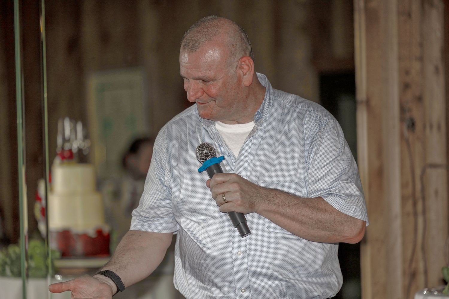 A person wearing white chef's attire holds a blue microphone while speaking indoors.