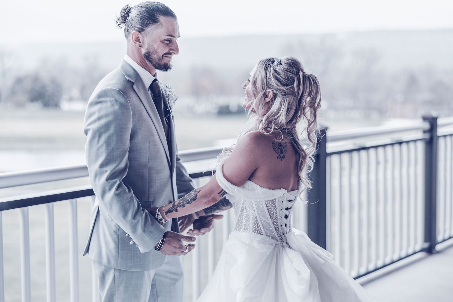 A bride and groom share an intimate moment together on a deck overlooking a misty waterfront landscape.