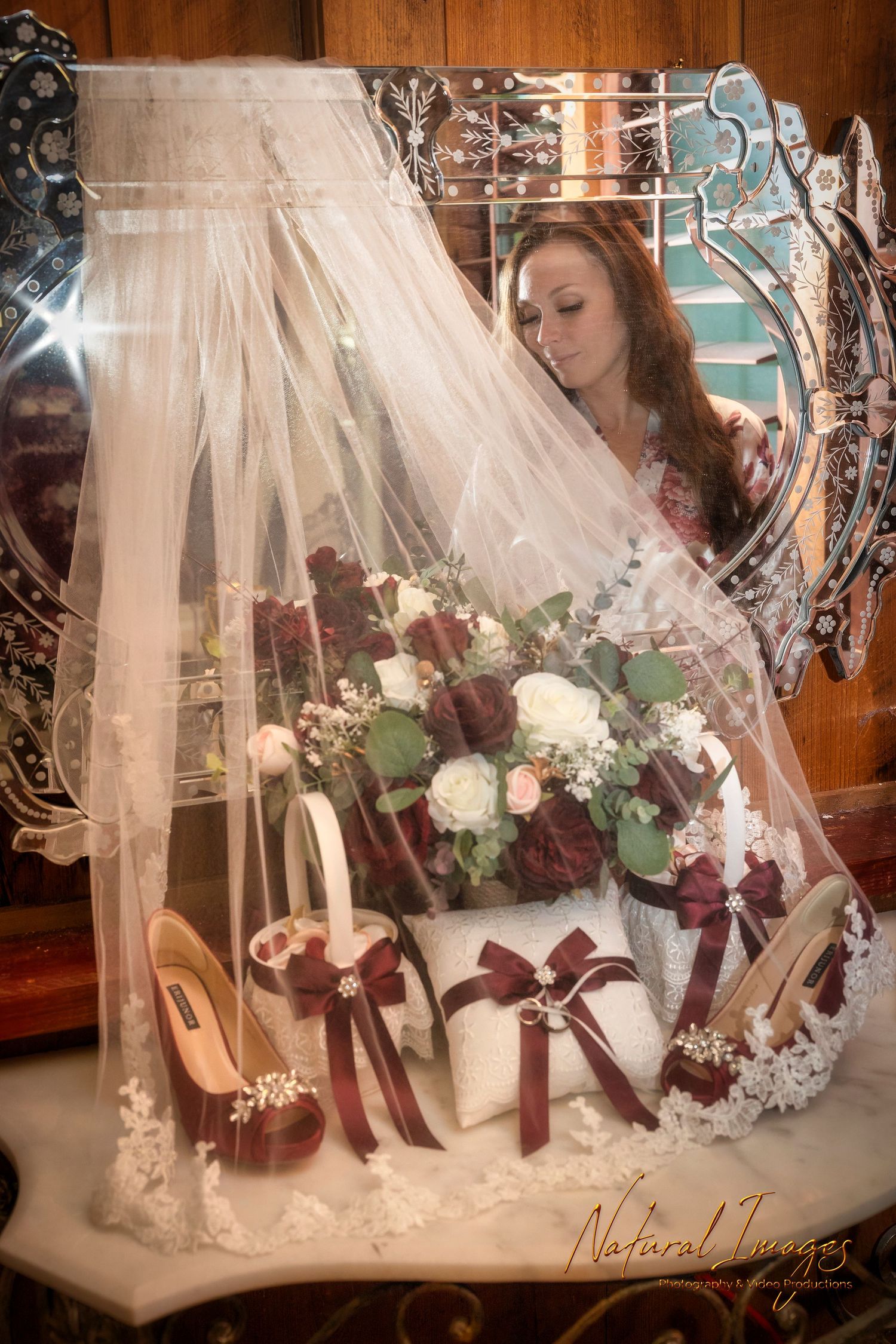 Wedding accessories display with white veil, burgundy bouquet, shoes and decor in ornate mirror.