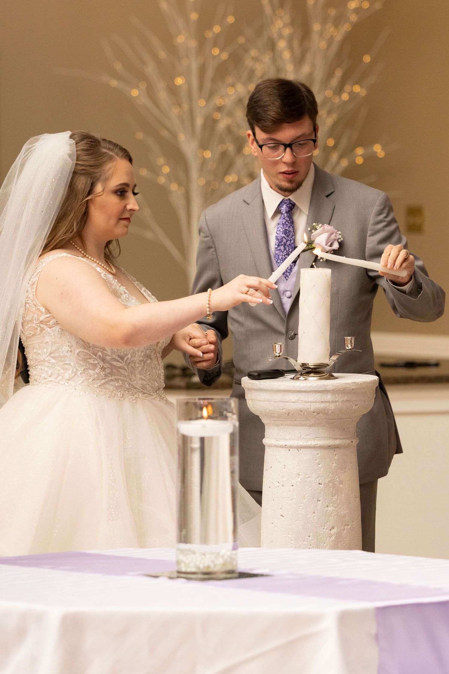 A couple performs a sand ceremony ritual at their wedding reception, pouring sand into a decorative vessel.