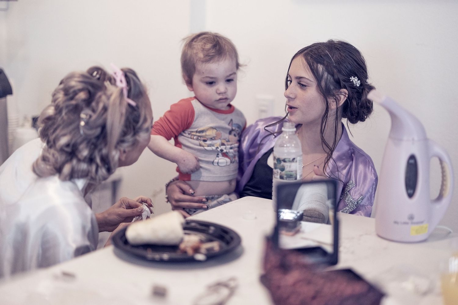 Three people gathered around a table with plates sharing what appears to be a homemade meal in a casual setting.