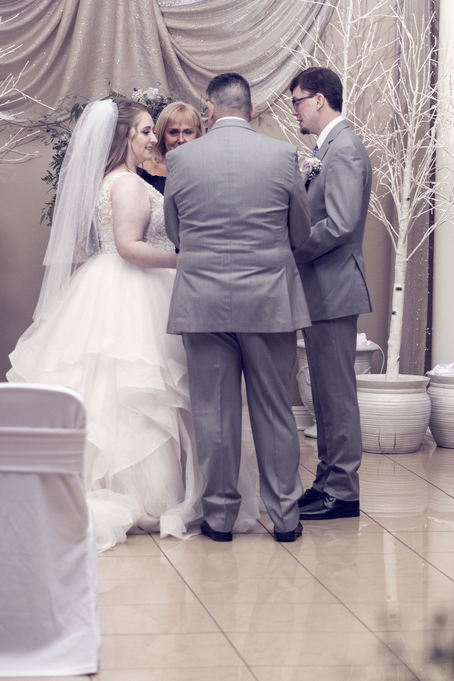 Wedding ceremony in elegant venue with white drapery and illuminated trees.