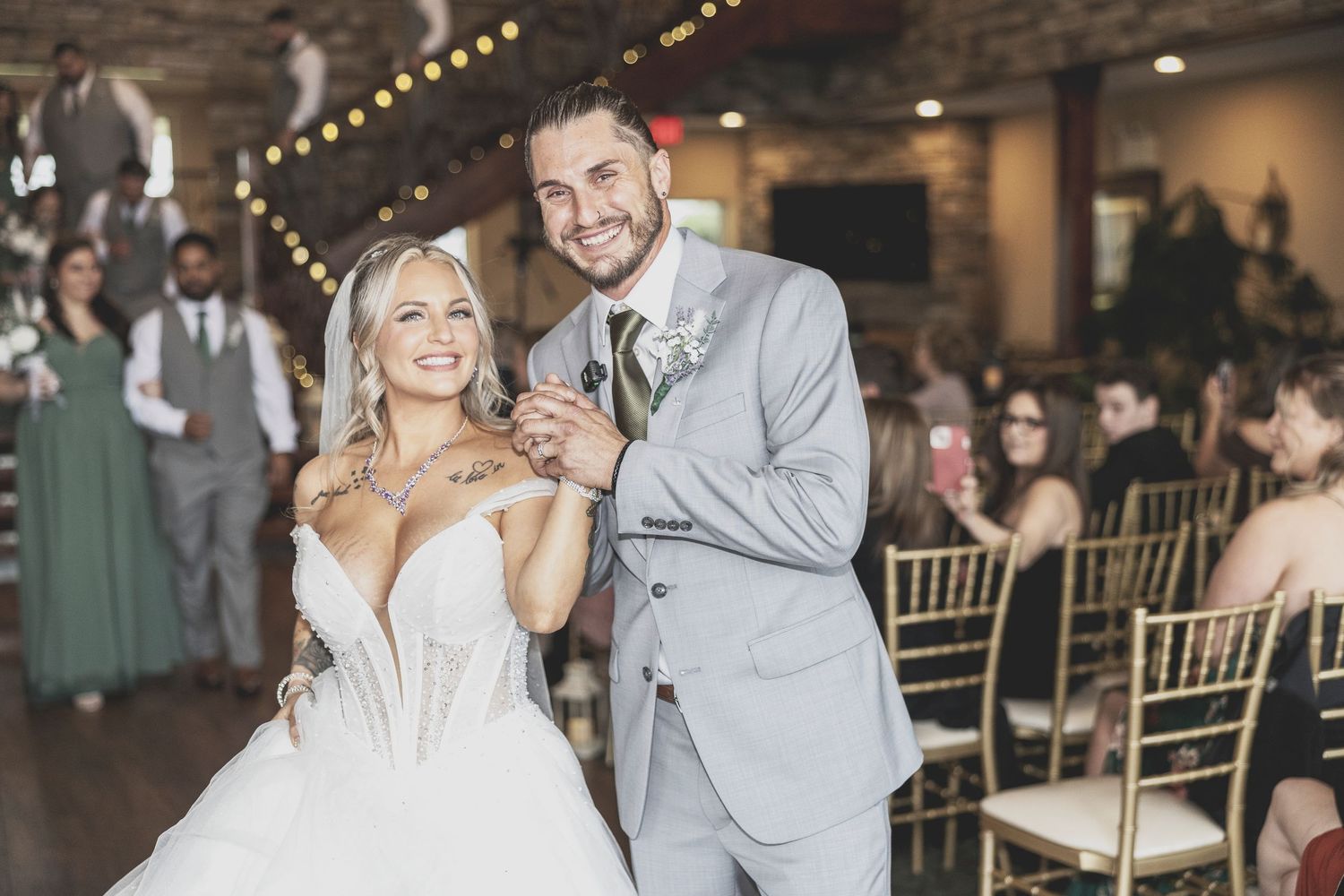 A couple shares their first dance at their wedding reception in an elegant rustic venue with string lights overhead.