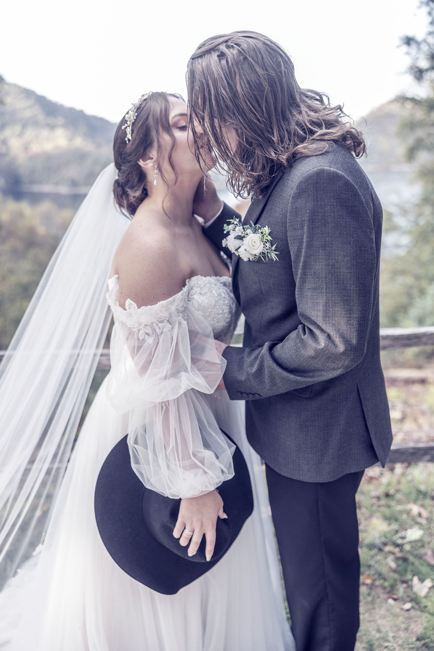 A romantic wedding couple in an ethereal mountain setting share a kiss, with the bride in white and groom in gray.
